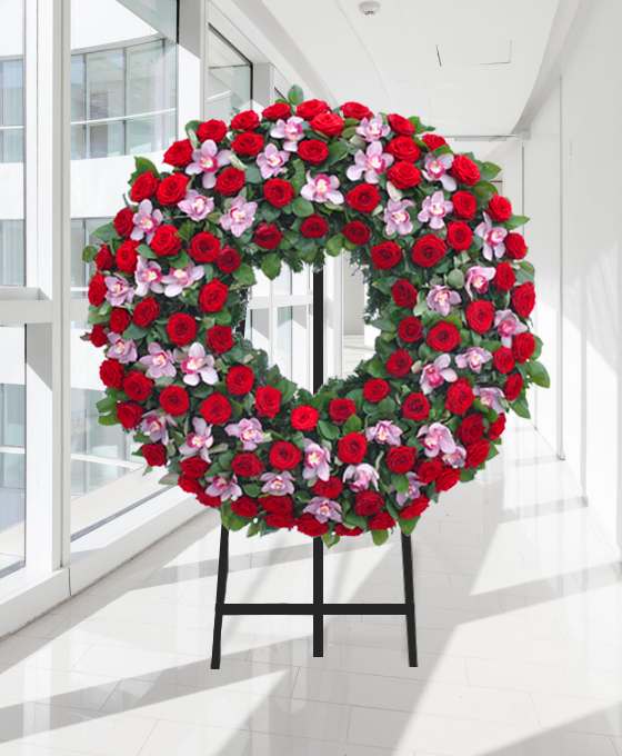 Coroa fúnebre circular de rosas vermelhas e flores rosadas, sobre tripé
