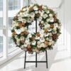 Coroa fúnebre circular de flores brancas e tons acastanhados, sobre tripé