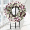 Coroa fúnebre circular de flores brancas e lilás, sobre tripé
