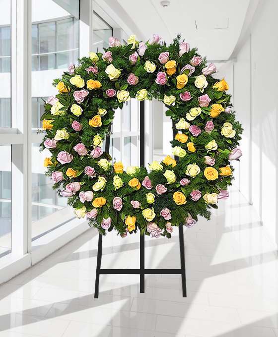 Coroa fúnebre circular de rosas amarelas, rosa e brancas, sobre tripé