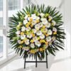 Composição fúnebre de margaridas brancas e flores amarelas com folhas de palmeira, sobre tripé