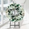 Coroa fúnebre circular de flores brancas com folhagem verde, sobre tripé