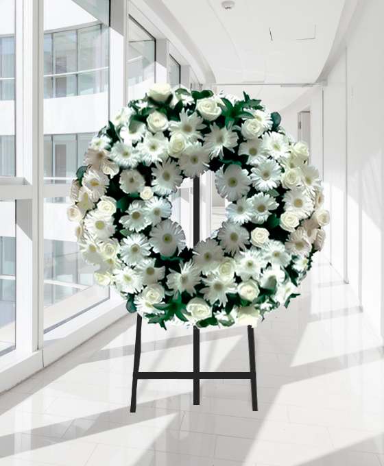Coroa fúnebre circular de flores brancas com folhagem verde, sobre tripé